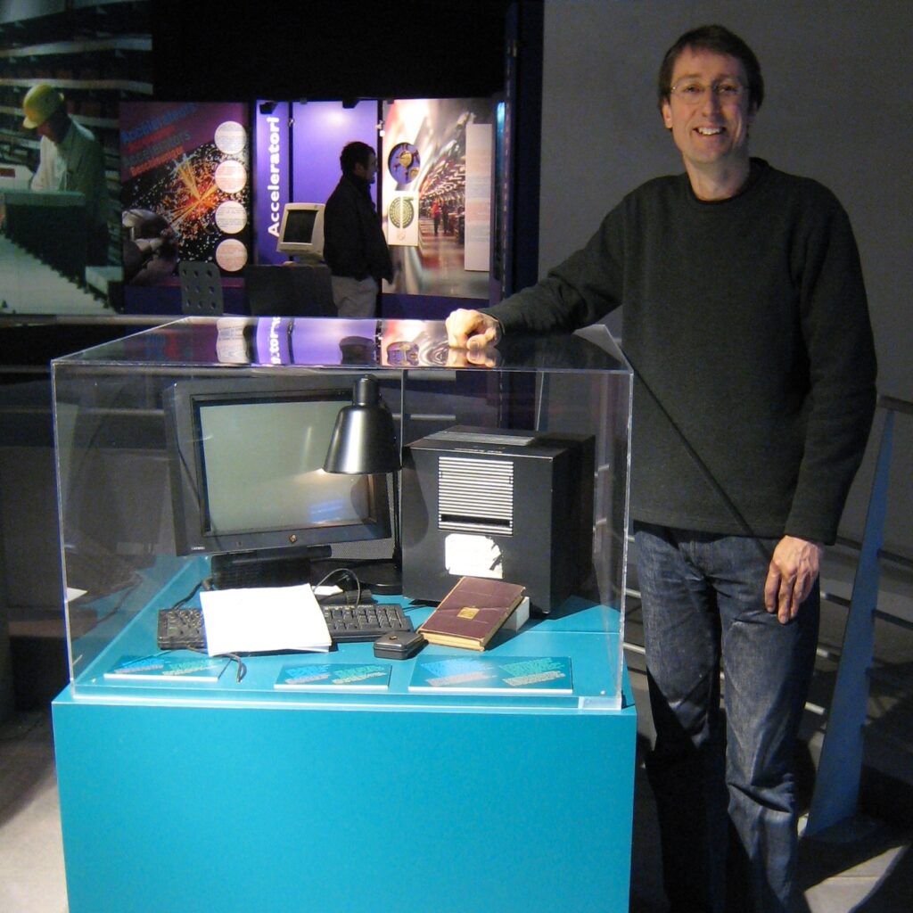 A man standing beside a museum case containing the first web server: Tim Berners-Lee's original NeXTcube