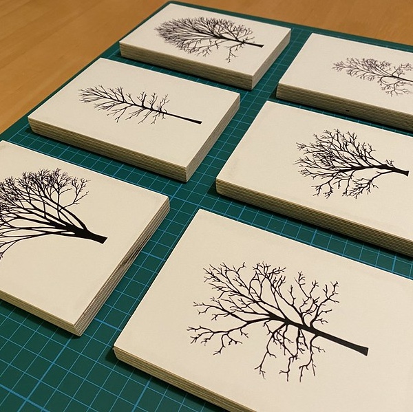 A set of 6 small mounted prints of silhouettes of trees arranged on a green cutting board on a table