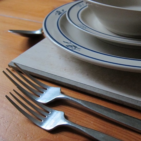 A stack of crockery on a bevel-edged placemat with some cutlery