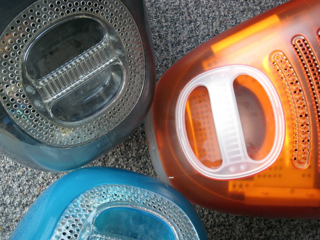 3 colourful iMacs sitting on a grey mottled carpet. Specifically: Graphite iMac 400 DV SE (1999); Tangerie iMac 333 (Rev. D, 1999); Indigo iMac 350 (2000).