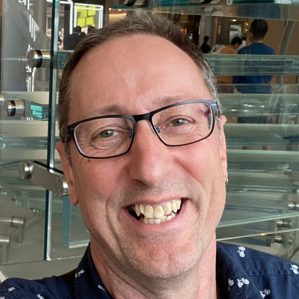 Headshot of a 60+ year-old man wearing glasses and smiling, head slightly tilted to the right.