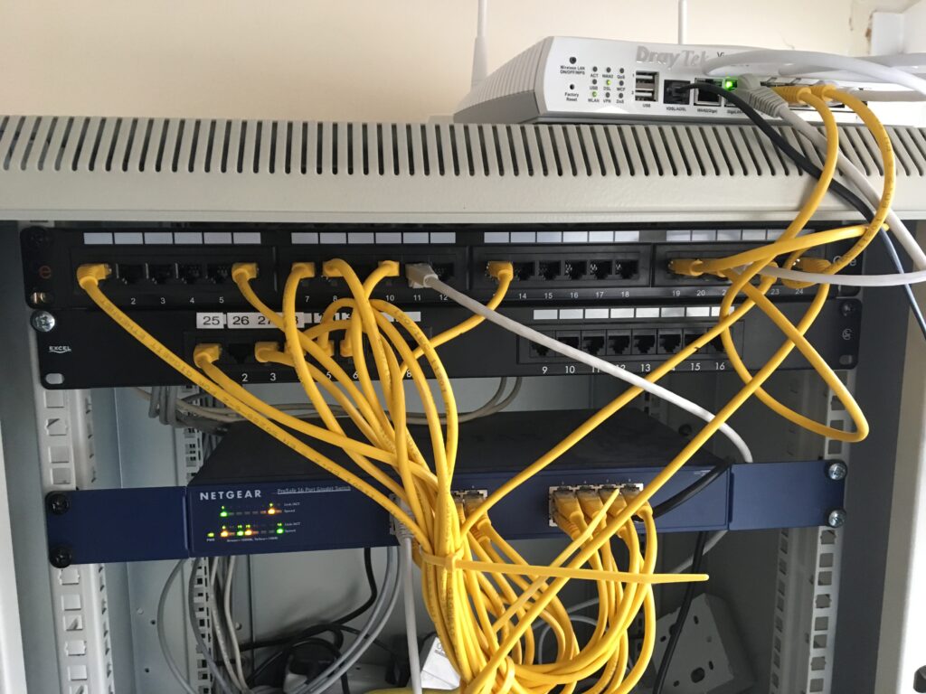 A comms rack with a switch, and router, and a number of mainly yellow patch cables.
